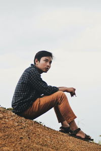 Side view of young man looking away against sky