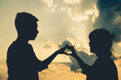 Silhouette couple making heart shape with hands against sky during sunset