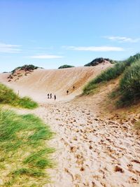 People walking on sand dune in field against sky