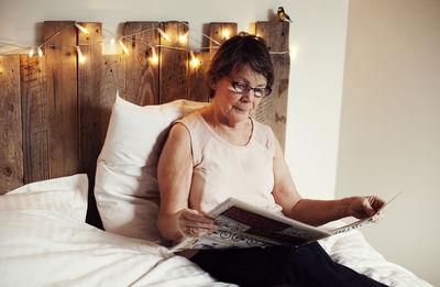 Senior woman reading newspaper in bed