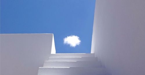 Low angle view of stairs and white wall against blue sky