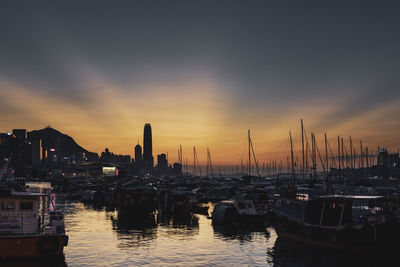 Boats moored in harbor at sunset