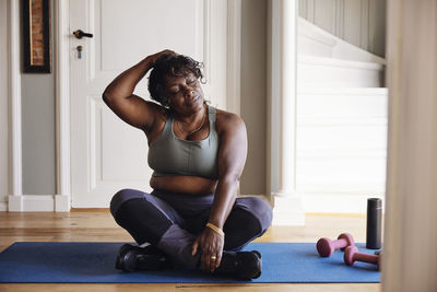 Mature woman with eyes closed stretching neck on exercise mat at home