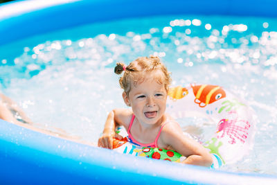 A laughing baby in a bright swimsuit learns to swim in the pool in the garden 