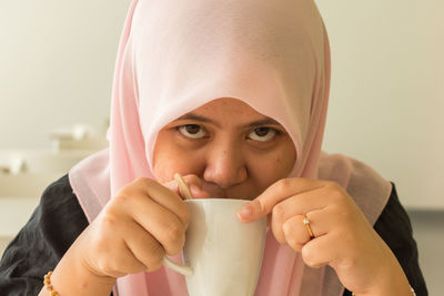 Portrait of young woman holding coffee cup against gray background