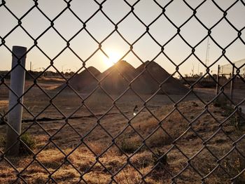 Chainlink fence on field against sky during sunset