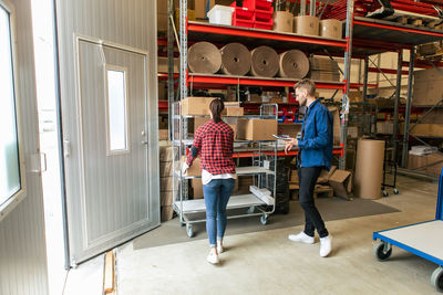 Manual worker looking at female colleague loading boxes on trolley at distribution warehouse