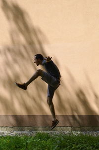 Side view of excited young man jumping against wall