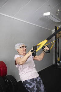 Active senior woman exercising on gymnastic rings at health club