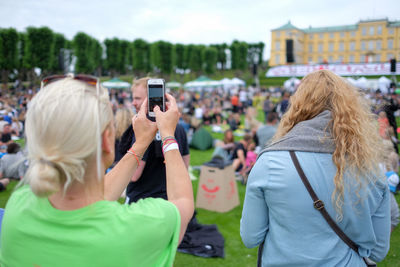 Rear view of woman photographing through smart phone at event