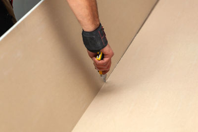 Cropped hand cutting plasterboard with work tool