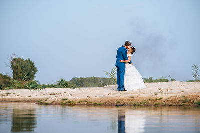 Couple kissing by lake against trees and sky