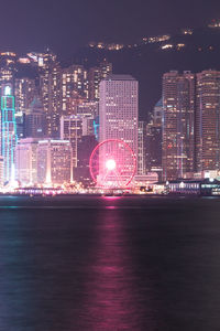 Illuminated buildings by sea against sky at night