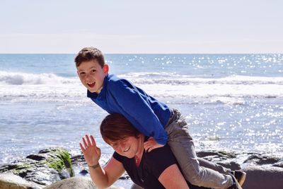 Portrait of happy mother with son at beach against sky