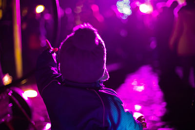 Rear view of boy standing on illuminated road at night