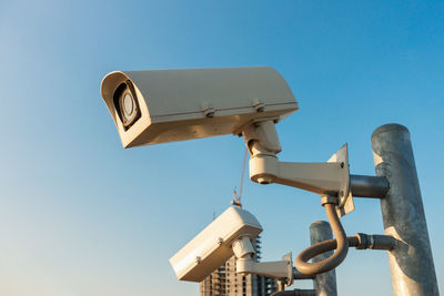 Low angle view of security camera against clear blue sky