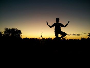 Silhouette of woman jumping at sunset