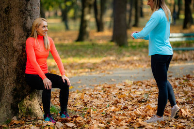 Women exercising outdoors in public park in the fall. trainer looking at woman doing squat hold.