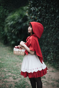 Full length of woman holding red basket while standing on field