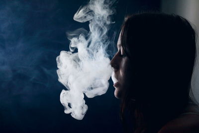 Side view of young woman smoking over black background