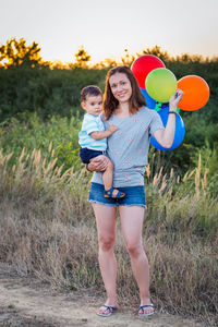 Portrait of happy woman carrying son and balloons on field