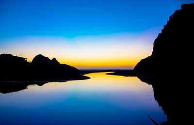 Reflection of silhouette trees in calm lake at sunset