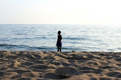 Rear view of boy standing on beach against clear sky