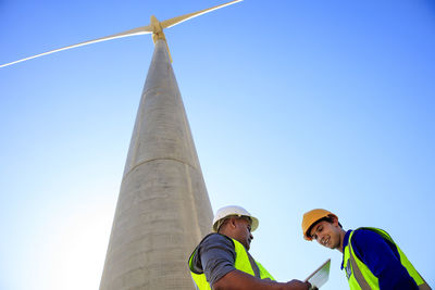 Low angle view of technicians with tablet in front of wind turbine