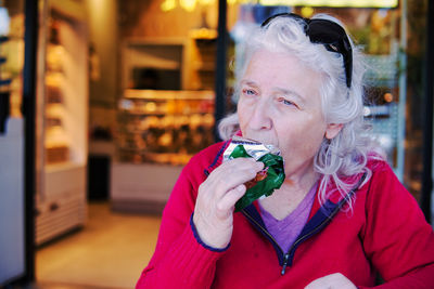 Woman eating snack bar in front of bakery shop.
