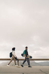 Side view of male and female friends walking on skateboards on road