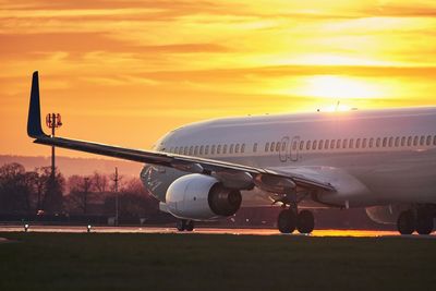 Airplane on airport runway against orange sky