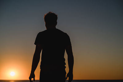 Silhouette man standing by sea against sky during sunset