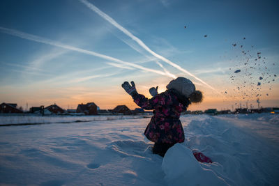 Full length of girl on snow covered land against sky during sunset