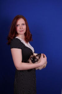 Portrait of beautiful woman with siamese cat against blue background
