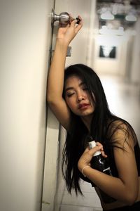 Beautiful woman leaning on door while holding beer bottle at home