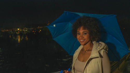 Portrait of woman with umbrella against sky at night