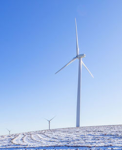 Wind turbines in a snow covered field with blue sky