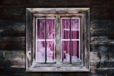 Close-up of closed window of old building with red and white checkered curtains