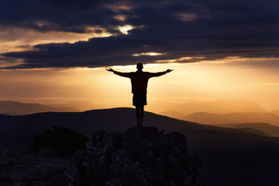 Silhouette man with arms outstretched standing on mountain at sunset