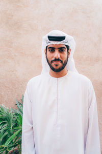 Portrait of young arabic man standing against beige wall