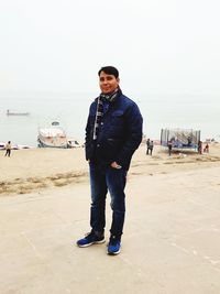 Full length portrait of young man standing on beach against sky