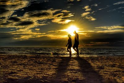 Silhouette couple walking on shore at beach during sunset