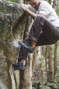 Full body of a male rock climber climbing a rock in a forest