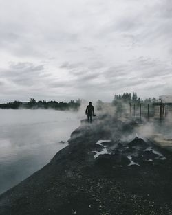 Rear view of man walking on rocky shore during foggy weather