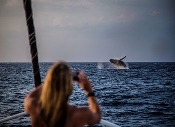 Rear view of woman photographing whale in sea against sky