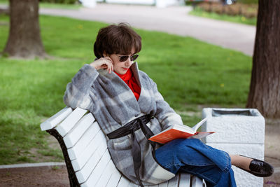 Young woman in the park reading a book while sitting on a bench
