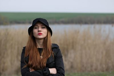 Portrait of beautiful young woman wearing hat standing on land