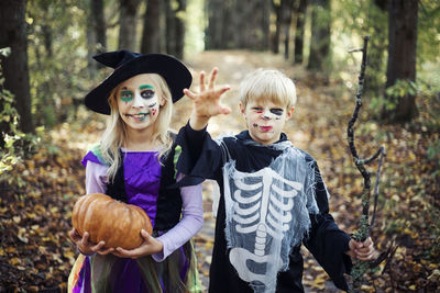 Portrait of halloween siblings standing in forest