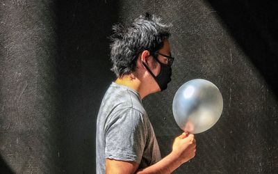 Portrait of young man holding gray balloon against wall.
