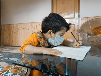 Boy wearing mask writing in book